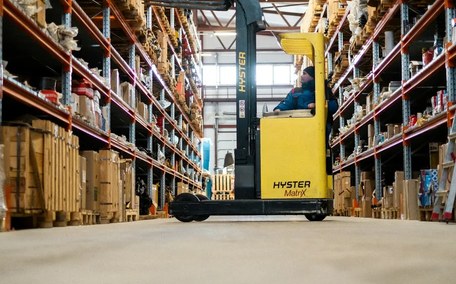 Warehouse operator driving a forklift past stocked pallet racking in a distribution depot