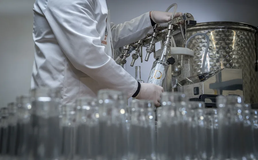 Technician in a lab coat operating a bottle filling line at a cosmetics manufacturing facility